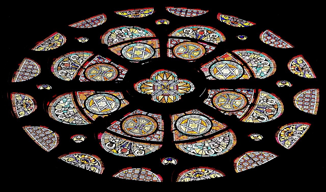 A circular stained-glass composition glows in many colored sections against a nearly black surrounding field.